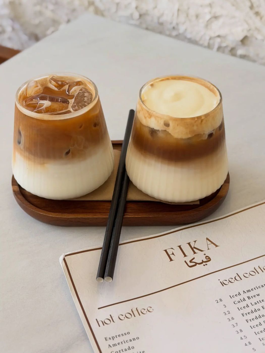 Two layered iced lattes on a wooden tray beside the FIKA menu